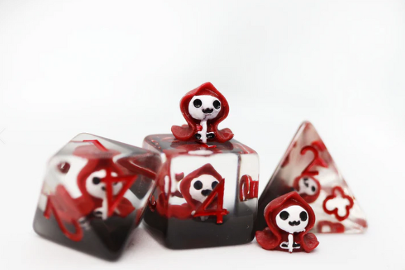 A detailed view of the Red Reaper RPG Dice Set by Foam Brain. The set includes a variety of dice, featuring designs of adorable skeleton characters in red hoods with a blend of red and black colors. Each die is intricately crafted with clear elements showcasing numbers and characters, perfect for tabletop gaming enthusiasts.