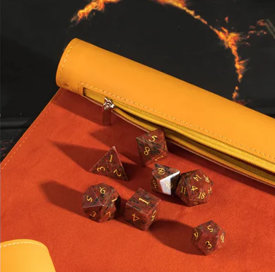 A vibrant Burn Yellow roll-up leatherette dice mat by Foam Brain, featuring a smooth yellow exterior and an orange interior. Displayed on the mat are various gaming dice in rich red and gold hues, showcasing diverse shapes including d20s and d10s, ideal for tabletop games.
