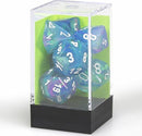 A clear plastic display case containing a set of colorful polyhedral dice in shades of blue and aqua. The dice have white numbers and are arranged inside the case, which features a black base and a light green backdrop, showcasing their vibrant colors. Ideal for tabletop gaming enthusiasts looking for premium dice.