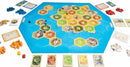 A vibrant board game setup for Catan: Seafarers, featuring hexagonal tiles representing land and sea, ships, settlements, and resources. Game pieces include blue and red ships and settlements, resource cards, dice, and development cards laid out on a colorful blue ocean background.