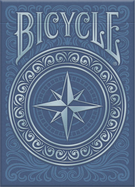 Bicycle Odyssey Card Deck created by US Playing Card Co. The card deck features an intricate blue design with a central compass motif surrounded by decorative swirls, ideal for card games and magic tricks.