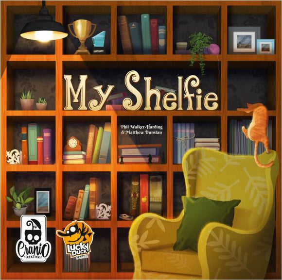 The board game 'My Shelfie' by Lucky Duck Games, featuring a colorful bookshelf filled with books, plants, and a decorative cat sitting on a chair. The game emphasizes creativity and strategy in arranging your bookshelf to create the best 'shelfie'.