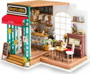 A detailed mini model of Simon's Coffee shop, featuring a charming exterior with a red awning and welcoming entrance. Inside, there's a well-equipped coffee counter, seating area with tables and chairs, a piano, and decorative plants, creating a cozy café atmosphere.