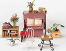 Simon's Coffee Model Kit by Robotime featuring a miniature piano with sheet music, a cozy chair, and various decorative plants and furniture elements.