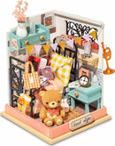 A detailed Sweet Dreams Bedroom Model Kit by Robotime, showcasing a cozy bedroom setup. The kit features a variety of miniature furniture, including a bed adorned with colorful pillows, a bear plush toy, books, candles, and decorative items. The walls and decor add a whimsical touch, with floral accents and playful banners, creating a charming and inviting atmosphere for creative DIY enthusiasts.