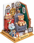 A beautifully detailed DIY holiday living room scene featuring a cozy armchair with a teddy bear, a small red table adorned with a cake topped with a cherry, a decorative green wall with framed pictures, and a side table with presents. The scene conveys warmth and a festive atmosphere, perfect for showcasing a creative and delightful holiday vibe.