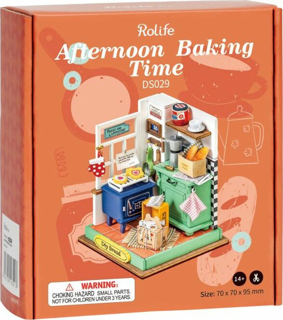 Robotime DIY Afternoon Baking Time kit featuring a colorful miniature kitchen scene. The box is adorned with illustrations of baking utensils and has a vibrant design. Inside, the setup includes a blue stove, green countertop, various baking supplies, and decorative items, ideal for creative DIY enthusiasts aged 14 and up.