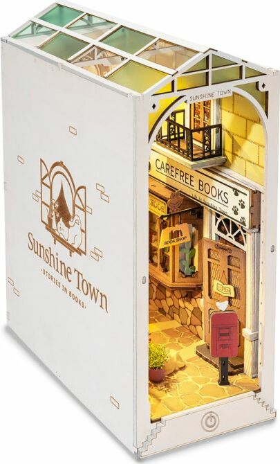 A detailed view of the Sunshine Town DIY Book Nook by Robotime. This charming miniature scene features a quaint bookstore named 'Carefree Books' with colorful decorations, a staircase, and a mailbox, inviting creativity and imagination in a cozy setting.