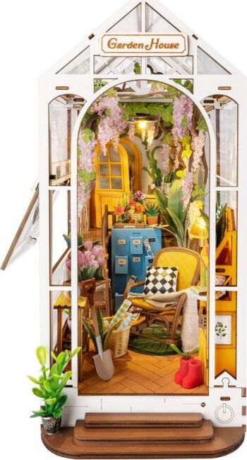 The Garden House DIY Book Nook is a charming miniature model featuring a cozy indoor garden scene. It includes details like vibrant flowers, a comfortable chair, colorful cabinets, and decorative elements. The design is intricate, showcasing a warm atmosphere with hanging plants and a stylish aesthetic, ideal for book lovers and DIY enthusiasts.