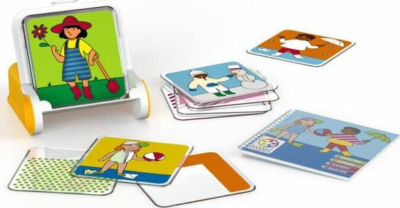 The Dress Code game by Smart Toys & Games features a fun, interactive mechanical puzzle set. It includes a stand with a colorful cartoon character holding a flower, accompanied by various illustrated cards showing different outfits and activities. The cards are placed around the stand, displaying playful images of children in seasonal clothing, engaging in sports, and enjoying various activities.