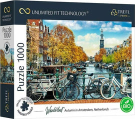 A beautifully illustrated 1000-piece jigsaw puzzle titled 'Wanderlust: Autumn in Amsterdam' by Trefl. The box features a picturesque Amsterdam canal scene, showcasing vibrant autumn foliage, historic buildings, and bicycles parked along the canal. The image captures the essence of fall in Amsterdam, with a clear sky and a tower in the background.