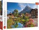 Trefl jigsaw puzzle titled 'Alps in the Summer', featuring a scenic view of picturesque Swiss houses alongside a serene river, surrounded by lush greenery and majestic mountains under a bright blue sky. The puzzle consists of 2000 pieces, ideal for nature lovers and puzzle enthusiasts.