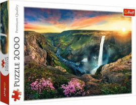 Trefl jigsaw puzzle featuring the stunning Háifoss Waterfall in Iceland. This 2000-piece puzzle showcases breathtaking scenery of the waterfall surrounded by lush hills, rocky cliffs, and colorful wildflowers under a vibrant sky at sunset.