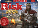 The game box of Risk Europe by Winning Moves, featuring the bold title 'Risk' in red letters. The artwork depicts a medieval king with a crown, standing confidently amidst a backdrop of smoke and fire from a battle scene, suggesting strategic warfare and conquest. Ideal for aged 14 and up, this enhanced version promises advanced rules and new gameplay variants.