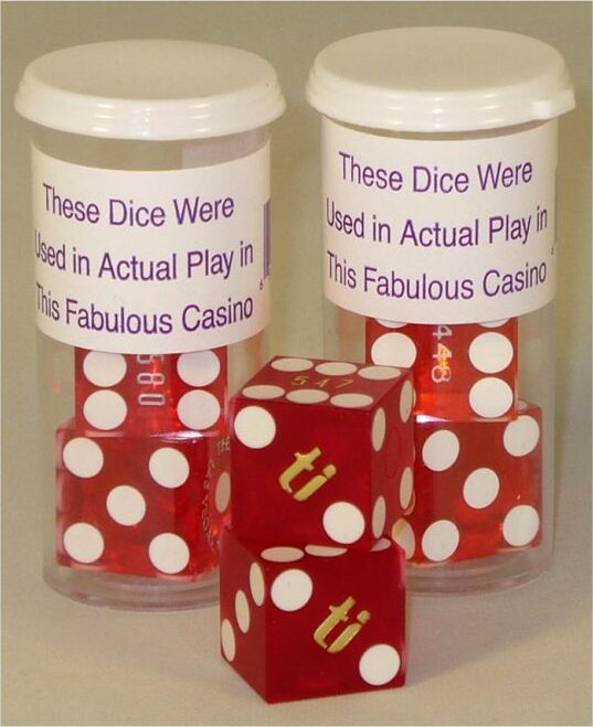 A Casino Precision Dice Set of 2 by WorldWise Imports, featuring two transparent containers filled with vibrant red dice. Each die is adorned with white dots and the labels state, 'These Dice Were Used in Actual Play in This Fabulous Casino.' The set's playful design and authentic casino history make it a perfect addition for gaming enthusiasts.