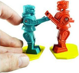 A hand holds one of the two colorful plastic robot figures from the World's Smallest Rock 'Em Sock, featuring a bright blue robot and a vibrant red robot, both poised to engage in a playful duel atop yellow bases.