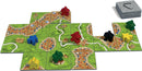 A vibrant game setup of Carcassonne by Z-Man Games, featuring colorful player pieces in red, yellow, green, and black placed on detailed landscape tiles depicting cities, roads, and fields. The game components include a neatly stacked set of tiles ready for play, showcasing intricate artwork and an engaging board layout for strategic gameplay.