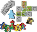 Mists Over Carcassonne board game by Z-Man featuring colorful character meeples, landscape tiles, and a blue ghost-shaped token. The game components are artfully arranged, showcasing the game's vibrant graphics and strategic gameplay elements.