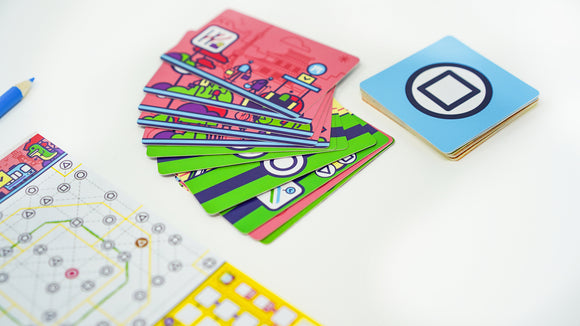 A vibrant game set titled 'Next Station Tokyo' featuring colorful cards and a game board. The components include a grid with a network design, a stack of illustrated cards showcasing various modes of transport, and a blue pencil for gameplay. The design is bright and engaging, perfect for family fun and strategic planning.