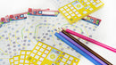 A vibrant tabletop scene featuring the game 'Next Station Tokyo' by Blue Orange U.S.A. Colorful game sheets displaying a map layout with various paths and symbols are scattered across the surface. Brightly colored pencils in shades of pink, blue, brown, and purple are positioned next to the game sheets, suggesting interactive gameplay. The game's design is playful and engaging, ideal for family fun and strategy sessions.