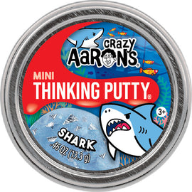 Mini Shark Thinking Putty by Crazy Aaron's in a silver tin. The putty is a light blue color with images of silver fish and a cartoon shark on the label, set against a colorful underwater scene.