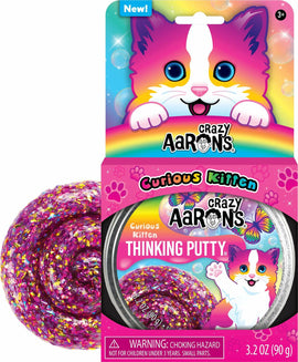 Crazy Aaron's Thinking Putty Curious Kitten kit features a vibrant pink and purple putty with sparkling glitter, shaped in a round container. The packaging shows a cute cartoon kitten with blue eyes and a rainbow background, highlighting the whimsical and colorful nature of the product. The kit is designed for ages 3 and up and promotes creativity and sensory play.