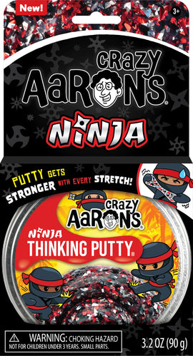 A pack of Crazy Aaron's Thinking Putty Ninja 4" in a clear container. The putty features a colorful black, red, and silver design. The packaging showcases a playful ninja character and includes a warning about choking hazards for children under 3 years, emphasizing its fun and stretchable qualities.