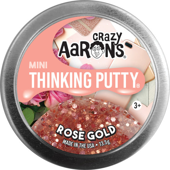 A round tin of Crazy Aaron's Mini Thinking Putty in Rose Gold color. The lid features the brand's logo and product name, with a shimmering putty displayed underneath. The background includes hints of pink roses and pastel colors, emphasizing the playful and creative nature of the product. Suitable for ages 3 and up.