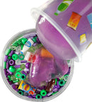 A close-up shot of Mini Mini Mart Slime Charmers from Crazy Aaron's Puttyworld. The image captures colorful beads and mini food and drink items embedded in a purple slime. The slime is being poured from a cup, showcasing a mix of vibrant textures and playful elements, perfect for sensory play.