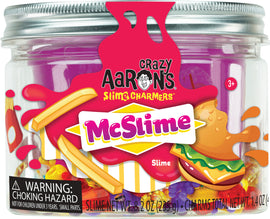 A jar of Crazy Aaron's McSlime Slime Charmers, featuring vibrant purple slime mixed with colorful charm pieces including food and fruit shapes. The jar is transparent with a silver lid, labeled with cheerful graphics and a warning about choking hazards for children under three years. The product is suitable for ages 3 and up.