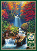 A beautifully illustrated jigsaw puzzle titled 'Mystic Falls in Autumn' by Cobble Hill. The scene features a vibrant autumn landscape with a cascading waterfall surrounded by colorful fall foliage. Various animals including deer and raccoons are depicted near the water and lush greenery, bringing the serene forest setting to life. The puzzle includes 1000 pieces and comes with a poster for reference.