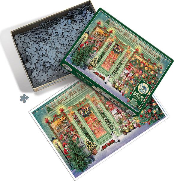 A colorful jigsaw puzzle depicting a charming Christmas flower shop scene by Cobble Hill. The box features a vibrant illustration of the shop filled with flowers, festive decorations, and holiday lights. The puzzle pieces are shown inside the box, alongside a depiction of the completed image.