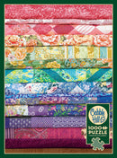 A colorful jigsaw puzzle titled 'Comfortable Rainbow' by Cobble Hill, featuring an array of vibrant fabrics stacked in a quilt pattern. It includes intricate floral designs and geometric shapes, designed for puzzle enthusiasts, containing 1000 pieces with a poster included for guidance.