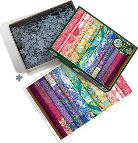 A colorful jigsaw puzzle titled 'Comfortable Rainbow' by Cobble Hill. The image shows an open puzzle box filled with interlocking pieces and a reference image of vibrant fabric patterns in multiple colors laid beside it.