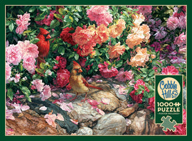 A colorful jigsaw puzzle featuring two cardinals among vibrant pink and yellow flowers. The design is intricate, filled with lush greenery and petals scattered on rocks, emphasizing nature's beauty. This 1000-piece puzzle by Cobble Hill also includes a poster.