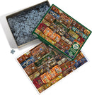 A Cobble Hill jigsaw puzzle featuring a colorful collage of vintage suitcases, displayed in an open box. The puzzle includes many intricate pieces scattered in the box, and a reference image of the completed puzzle showing a vibrant arrangement of different suitcase designs, with labels and stickers adding character.
