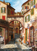 A vibrant and colorful jigsaw puzzle featuring a picturesque Tuscan street scene, showcasing charming buildings with red brick facades, green shutters, and various shops. The cobblestone path leads through the town, with outdoor seating at a pizzeria and beautifully displayed ceramics, creating an inviting atmosphere.