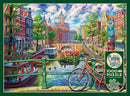 A vibrant jigsaw puzzle depicting a picturesque Amsterdam canal scene, featuring colorful buildings, a bridge, and a bicycle in the foreground. The image showcases lush greenery, boats on the water, and people enjoying the scenery, capturing the charm of the city. The puzzle includes 1000 pieces and a poster for reference, made by Cobble Hill.