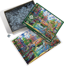 Cobble Hill 1000-piece jigsaw puzzle featuring a vibrant Amsterdam canal scene. The box is open, showcasing numerous puzzle pieces and a colorful image of bicycles by the water, charming houses, and lush greenery.