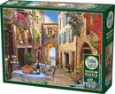 Cobble Hill French Village jigsaw puzzle featuring a quaint street scene. The artwork displays charming tables set with floral arrangements and wine bottles, framed by colorful buildings adorned with vibrant flowers. The puzzle contains 1000 pieces and includes a poster for reference.