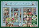 A beautifully illustrated jigsaw puzzle titled 'Parisian Flowers' by Cobble Hill. The image showcases a charming flower shop with a variety of floral displays in pots and vases, featuring vibrant blooms in a quaint storefront setting. A small dog stands by the entrance, adding a whimsical touch to the scene. The puzzle includes 1000 pieces and comes with a poster.