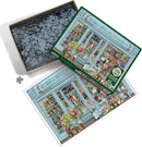 A vibrant jigsaw puzzle titled 'Parisian Flowers' by Cobble Hill. The image shows the puzzle box featuring a beautifully illustrated flower shop with colorful floral arrangements, shop windows, and a cute dog. The box is open, revealing numerous interlocking puzzle pieces inside and an image reference of the completed puzzle.