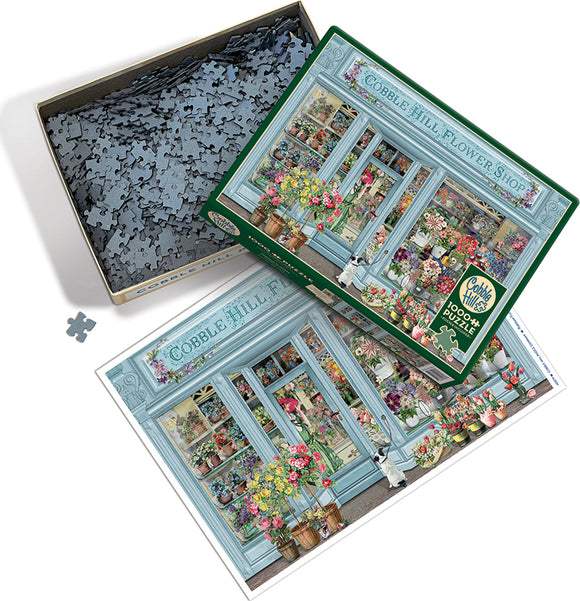 A vibrant jigsaw puzzle titled 'Parisian Flowers' by Cobble Hill. The image shows the puzzle box featuring a beautifully illustrated flower shop with colorful floral arrangements, shop windows, and a cute dog. The box is open, revealing numerous interlocking puzzle pieces inside and an image reference of the completed puzzle.