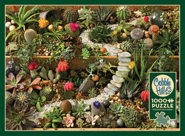 A vibrant jigsaw puzzle featuring a succulent garden overflowing with various cacti, succulents, colorful flowers, and small ornamental stones. The intricate details of the plants showcase a rich variety of textures and colors, inviting nature enthusiasts to piece together this beautiful scene. The Cobble Hill brand logo is featured prominently on the packaging, highlighting that this is a 1000-piece puzzle that includes a poster for reference.