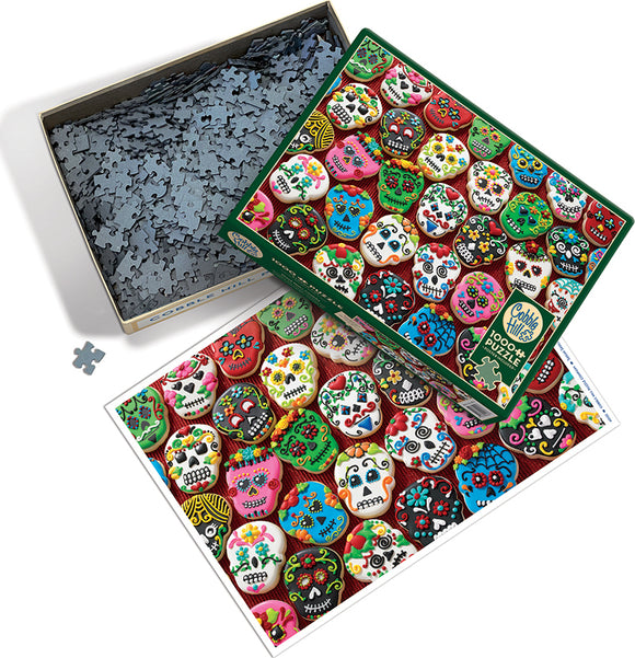 A colorful jigsaw puzzle featuring an assortment of sugar skull cookies, decorated with vibrant icing and floral patterns, displayed on the box lid. The puzzle pieces are spread out in a box, showcasing a distinct and festive design perfect for puzzle enthusiasts and lovers of Día de los Muertos.