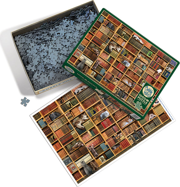 The Cat Library jigsaw puzzle by Cobble Hill, featuring a detailed image of a bookshelf filled with colorful books and playful cats. The puzzle box is open, with pieces scattered and a visual reference of the completed puzzle beside it.