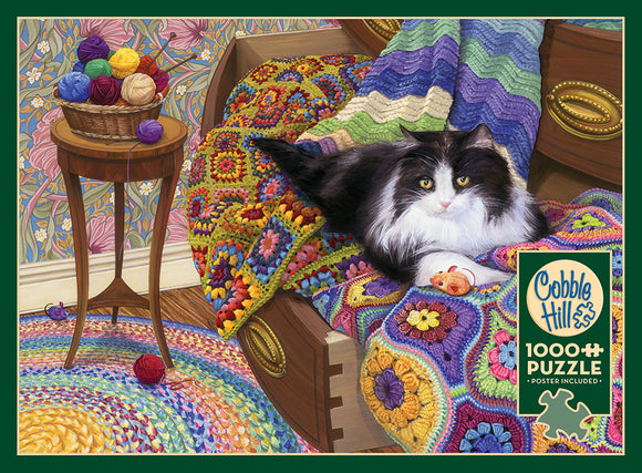 A 1000-piece jigsaw puzzle titled 'Comfy Cat' by Cobble Hill, featuring a cozy scene with a black and white cat lounging on a colorful crocheted blanket. Surrounding the cat are vibrant yarn balls in a basket, with intricate floral wallpaper in the background, creating a warm and inviting atmosphere.