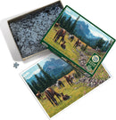 The Horse Meadow jigsaw puzzle by Cobble Hill features a scenic landscape image with horses grazing in a vibrant meadow surrounded by mountains and trees. The puzzle box is open, showcasing the numerous interlocking pieces inside, alongside the completed image of the puzzle.
