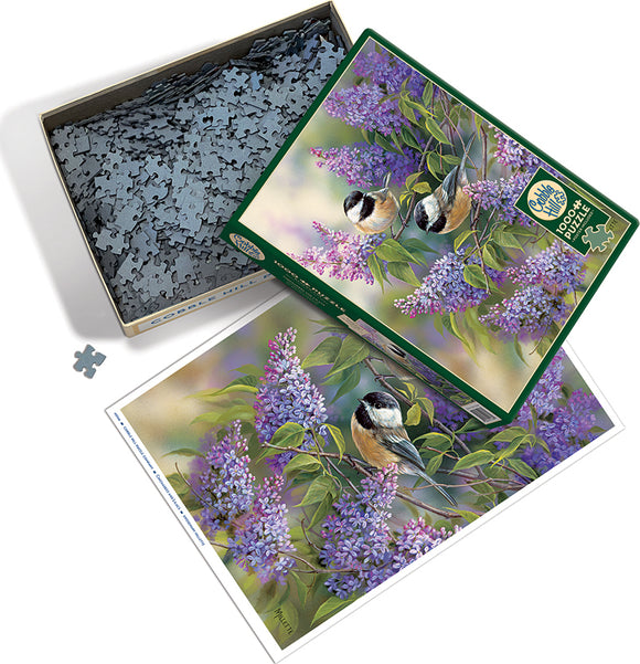 A colorful jigsaw puzzle titled 'Chickadees and Lilacs' by Cobble Hill. The box contains numerous intricately shaped pieces inside, alongside an image of the completed puzzle featuring vibrant lilacs and charming chickadee birds.