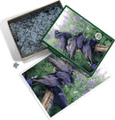 Cobble Hill jigsaw puzzle titled 'Raven Rendezvous'. The image shows a beautifully detailed illustration of ravens perched on a log among purple flowers. The puzzle box is opened, revealing numerous gray jigsaw pieces. A completed image of the puzzle is positioned next to the box, showcasing the serene scene of nature.